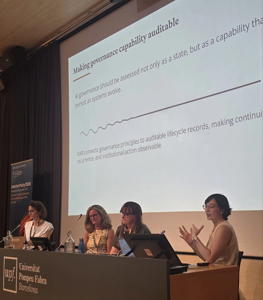 Marisa Vasconcelos presents NIAR-Saúde’s work at Data for Policy 2026, with the FIAR slide projected behind her